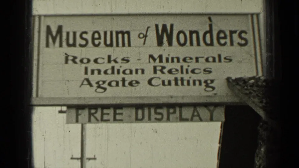 Black-and-white 8mm frame from Bend, Oregon showing the Museum of Wonders sign with exhibit text above a Free Display board.