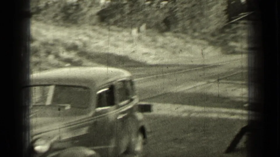 1937 Bend, Oregon home-movie frame showing a 1930s sedan moving along a rural road in soft black-and-white focus.