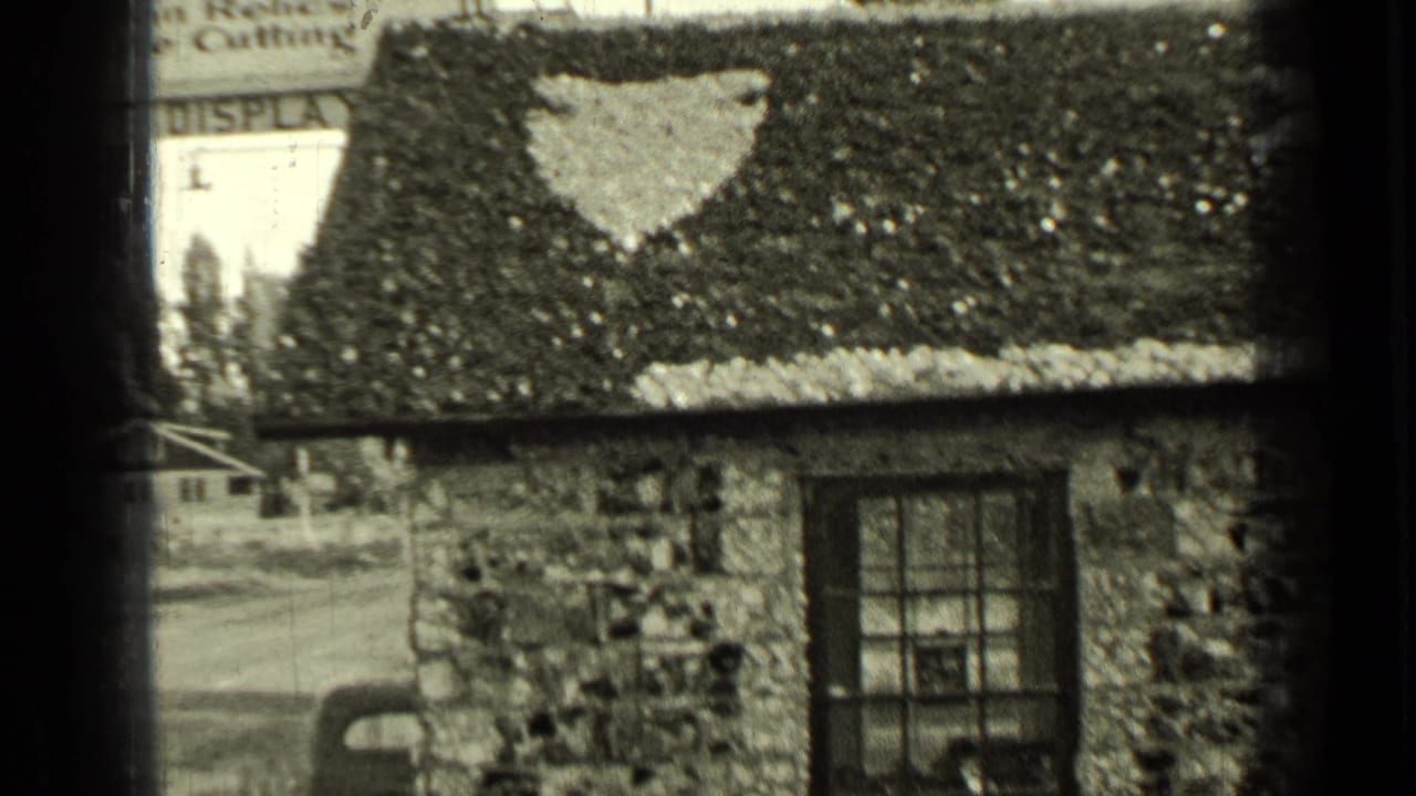 Small stone house with a star shape painted on the roof and a partial roadside sign behind it.