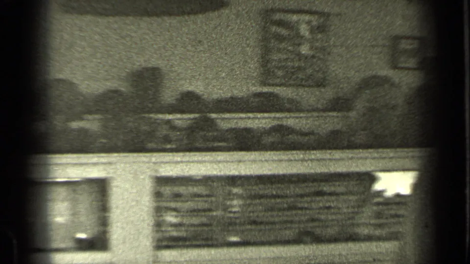 Soft 1937 Bend, Oregon home-movie frame showing a dim, partially obscured view with signage or display elements behind a dark window frame.