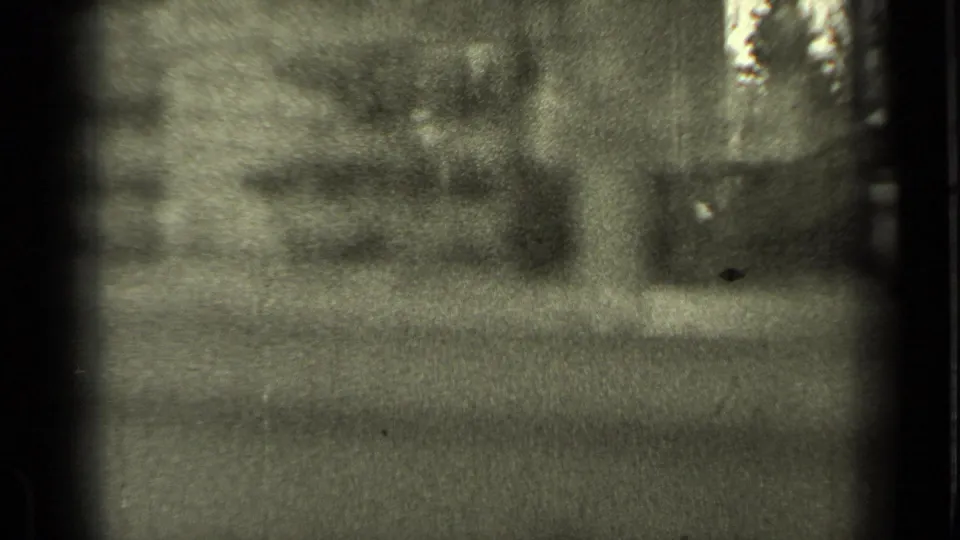 Grainy 1937 Bend, Oregon home-movie frame with a dim window view and a partially obscured person near the glass.