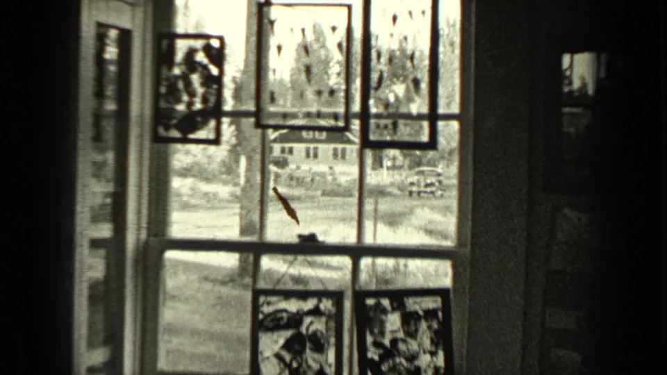 1937 Bend, Oregon home-movie frame looking through a decorated window toward a residential street and parked or moving car.