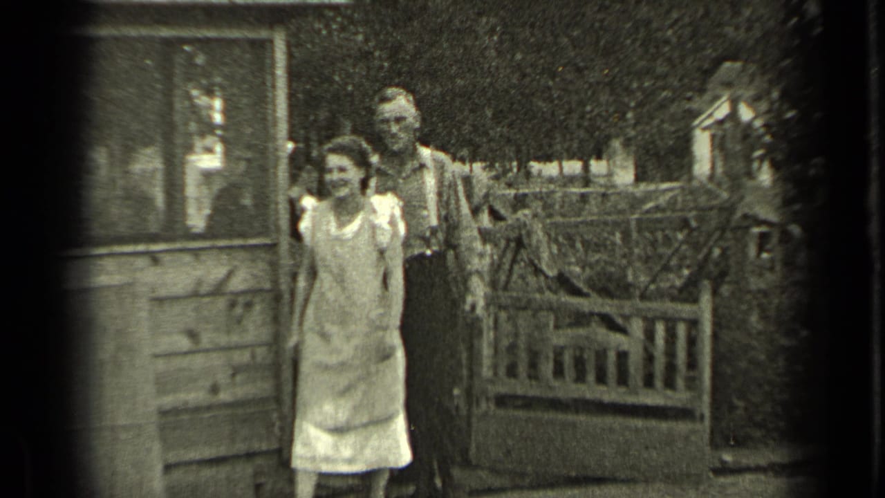 Young woman and man standing outside beside a wooden house and gate.