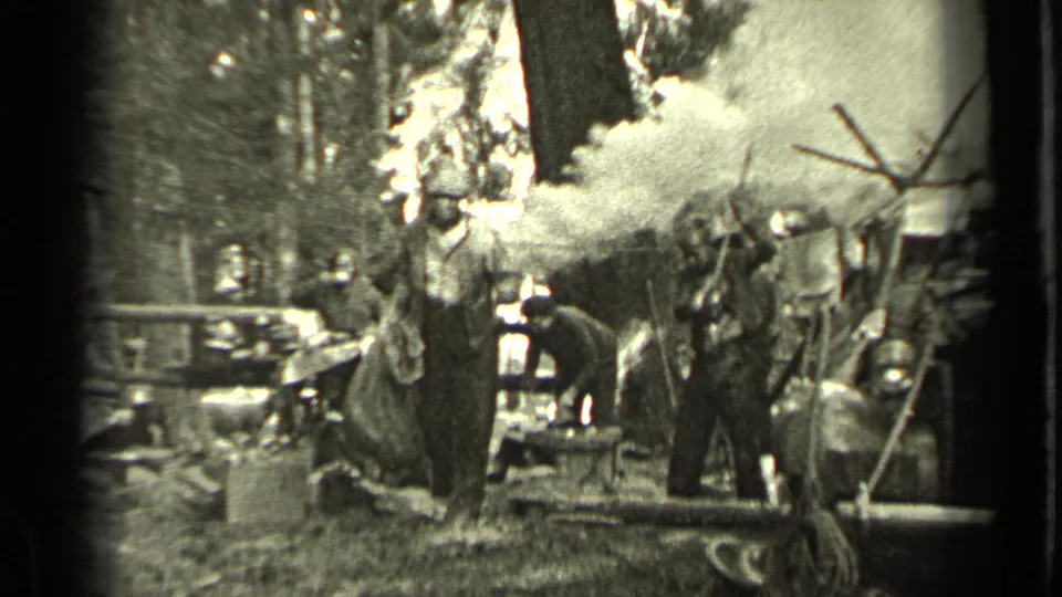 Men in work clothes appear to pack or manage gear at a smoky wooded campsite near Bend, Oregon in the 1937 home movie.