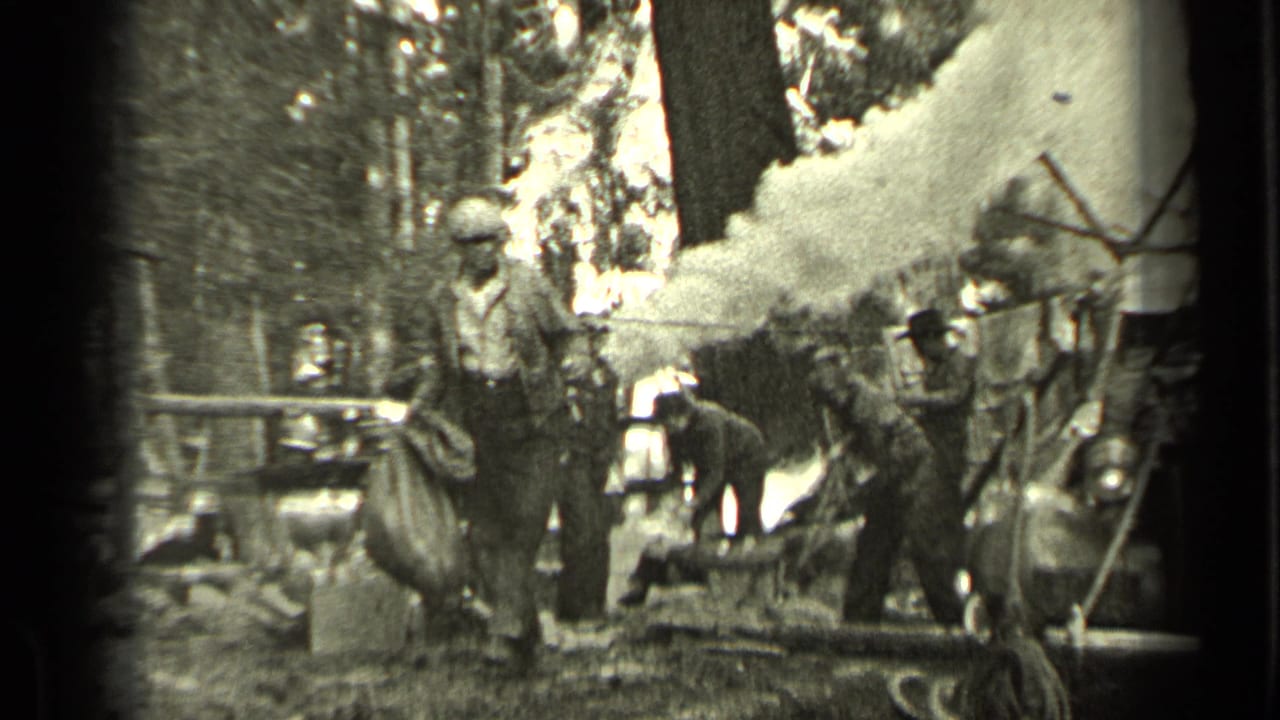 In Bend, Oregon, 1937, a man in work clothes carries a large sack past a smoky wooded campsite with adults and a dog nearby.
