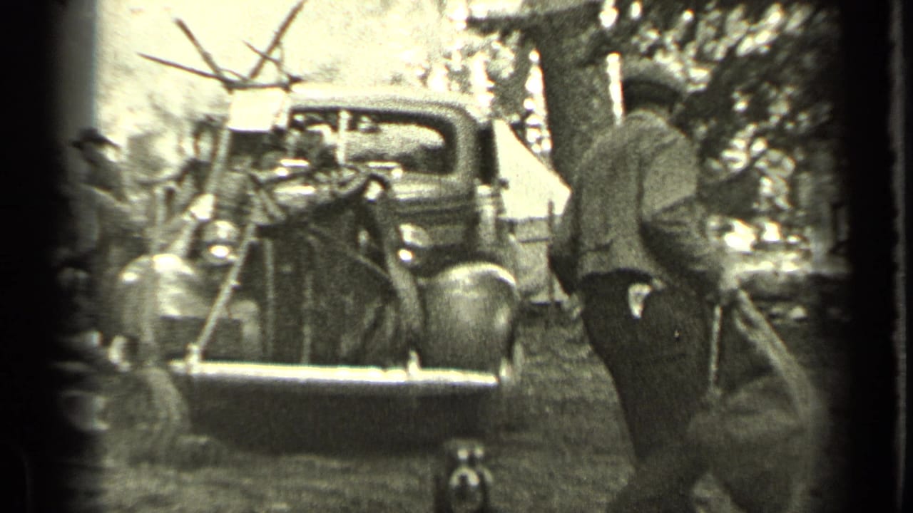 Man carries a large bag toward a vintage truck at a wooded campsite.
