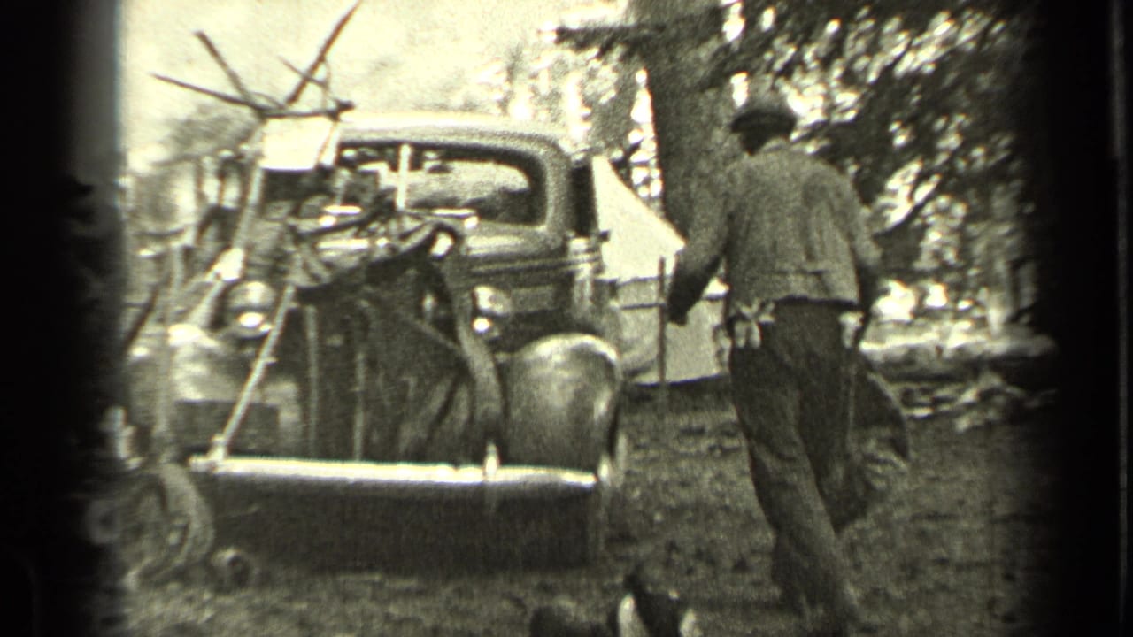 Man walks away from a vintage truck with camp gear and a tent nearby.