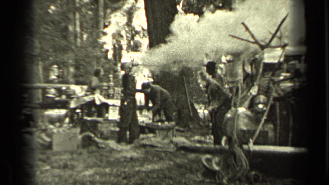 1937 Bend, Oregon campsite frame with a man near a smoky area, other adults nearby, and trees surrounding the scene.
