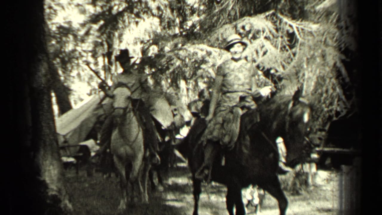 A group of riders on horses, some with visible hats, moves through a wooded Bend, Oregon setting with camp equipment in view.