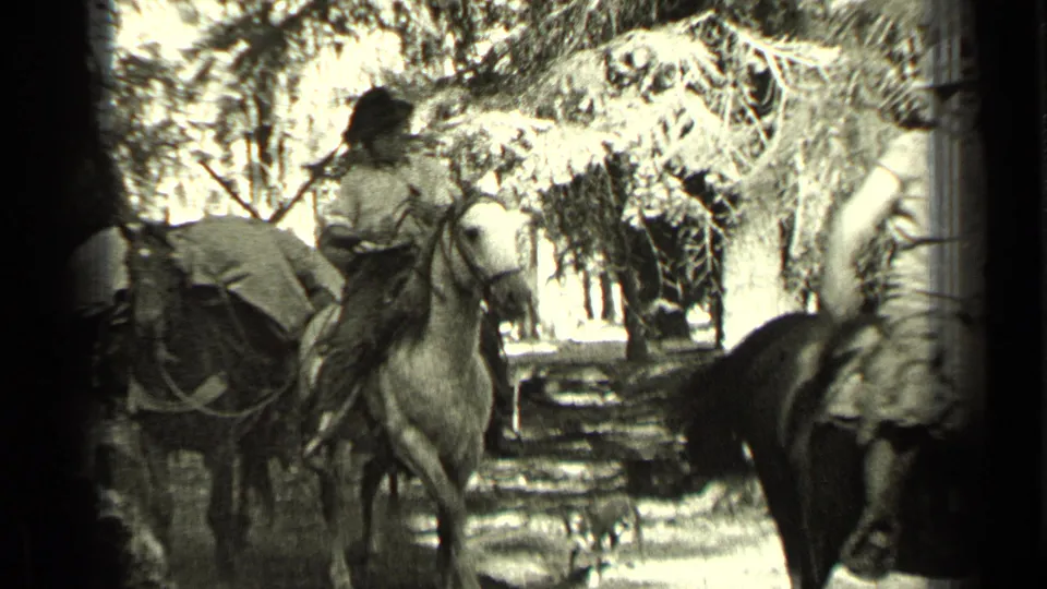 A rear view of a rider on a light-colored horse appears among pack animals and trees in the 1937 Bend, Oregon home-movie footage.