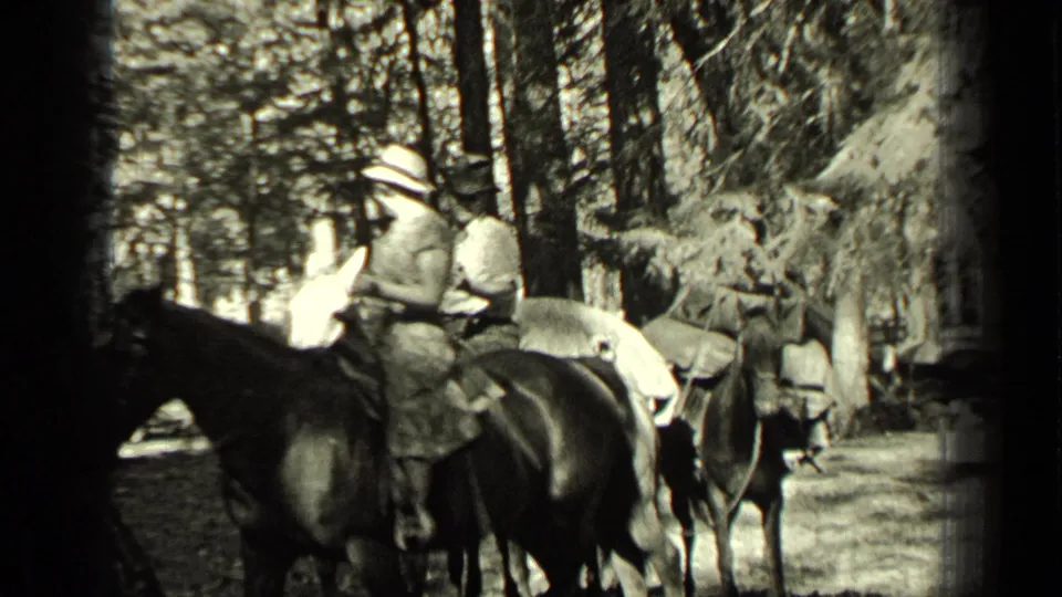 The 1937 8mm frame shows the two horseback riders from a closer angle, with the dark horse crossing the foreground and trees behind them.