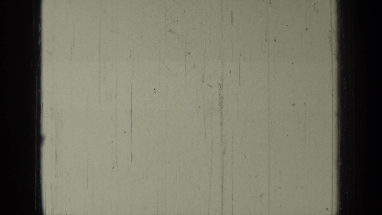 Pale monochrome frame with dark borders, scratches, and little visible landscape detail.