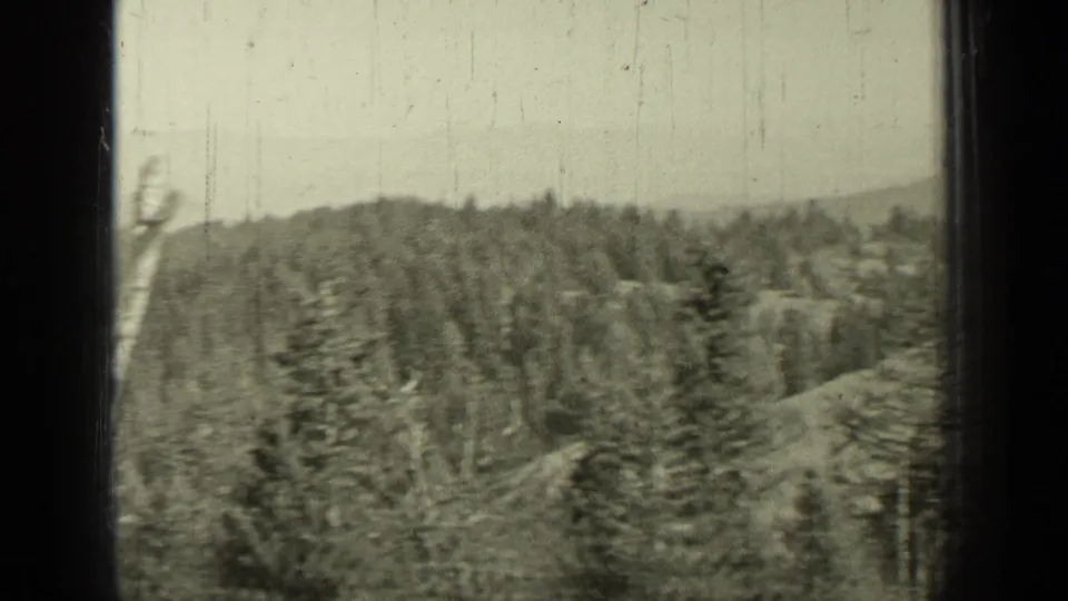 1937 Bend, Oregon home-movie view of evergreen-covered rolling hills beneath a pale sky, framed by dark 8mm gate edges.