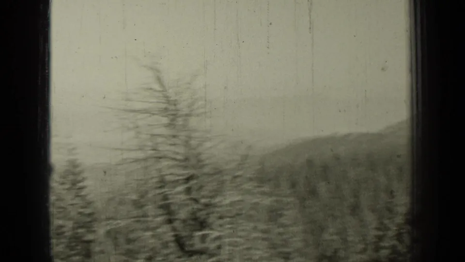 Bend, Oregon 1937 frame with motion-blurred forested hills and a tall roadside tree or pole within visible 8mm gate edges.