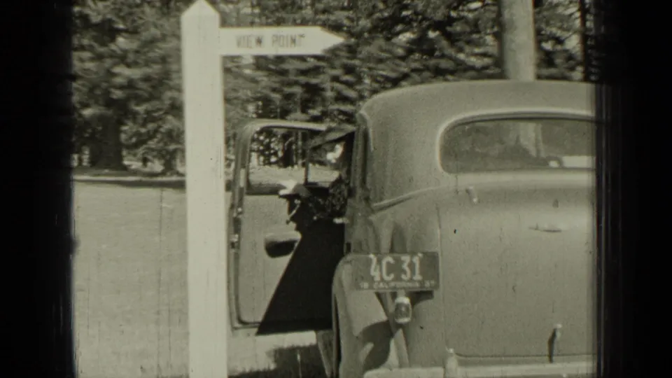 Bend, Oregon 1937 roadside view with a white viewpoint sign, parked 1930s cars, an open door, trees, and a readable license plate.