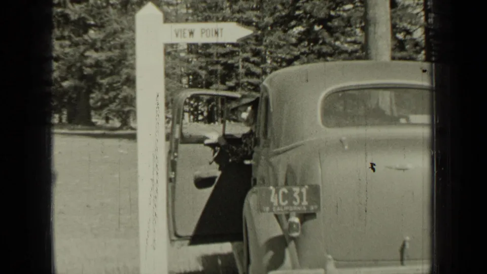 Bend, Oregon 1937 frame showing a viewpoint sign, rear of a 1930s car, open door, wooded background, and visible plate detail.