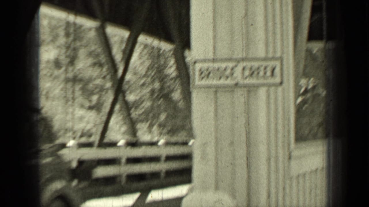 Soft 8mm frame from the Oregon travel clip showing bridge structure, a sign, and a passing automobile.