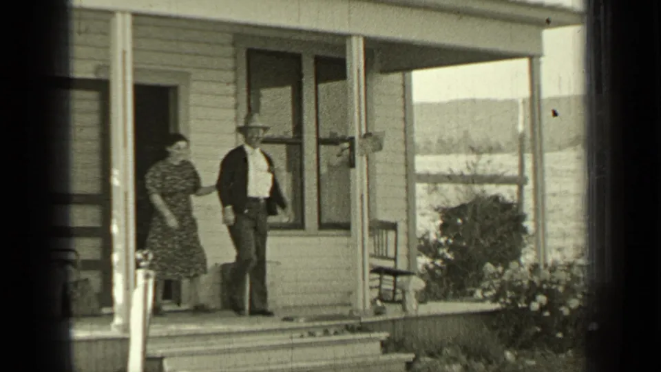 In Bend, Oregon, 1937 home-movie footage, a man in a hat and a woman in a patterned dress stand on a farmhouse porch.