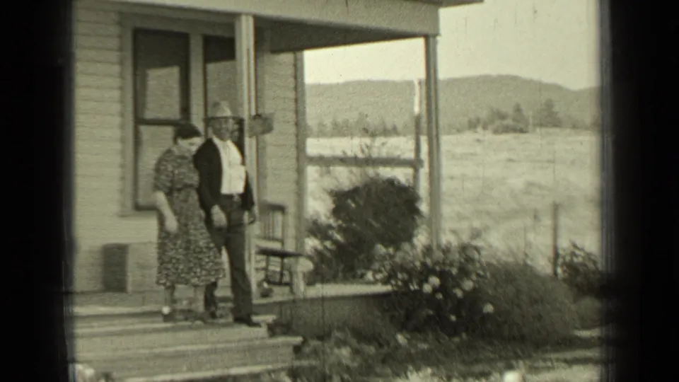 The couple begins leaving the farmhouse porch in rural Bend, Oregon, with low bushes, fence posts, fields, and hills behind them.