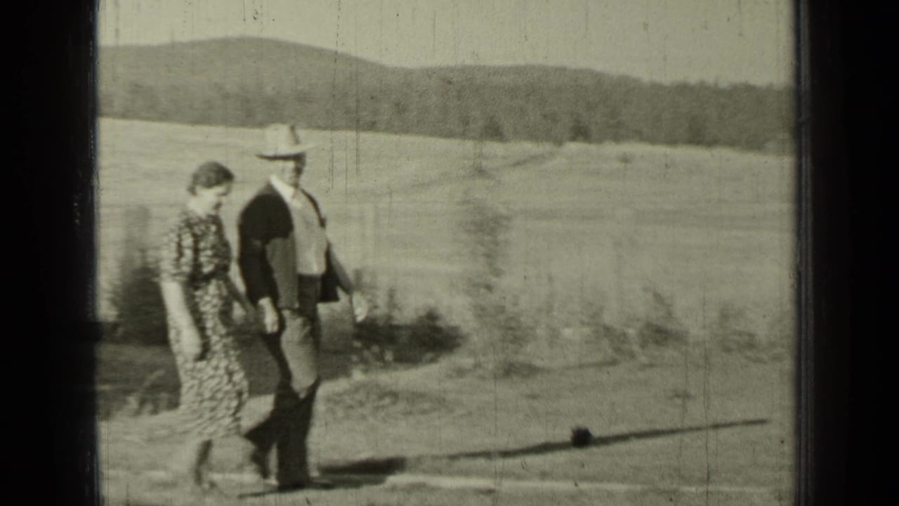 Man in a fedora and woman in a patterned dress walk across an open field.