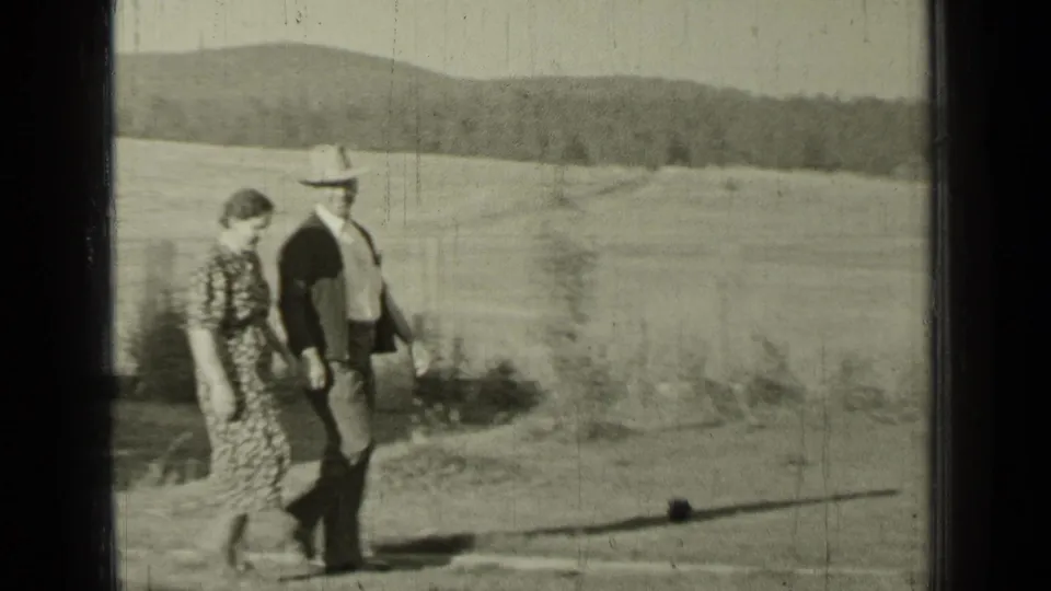 In Bend, Oregon, 1937, two adults walk through a rural field, with rolling hills visible behind them.