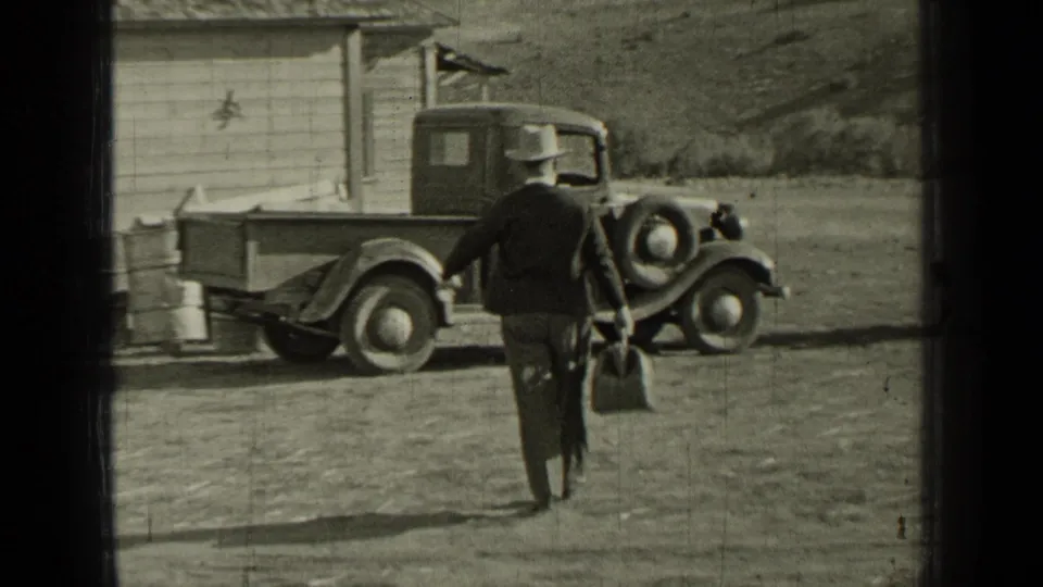 A man in a hat approaches a 1930s pickup parked near a wooden outbuilding in rural Bend, Oregon.