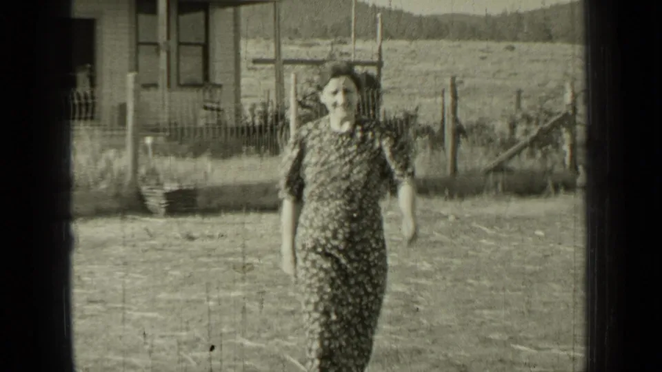 The woman comes closer to the camera in the Bend, Oregon home movie, with a fence, field, and house edge behind her.