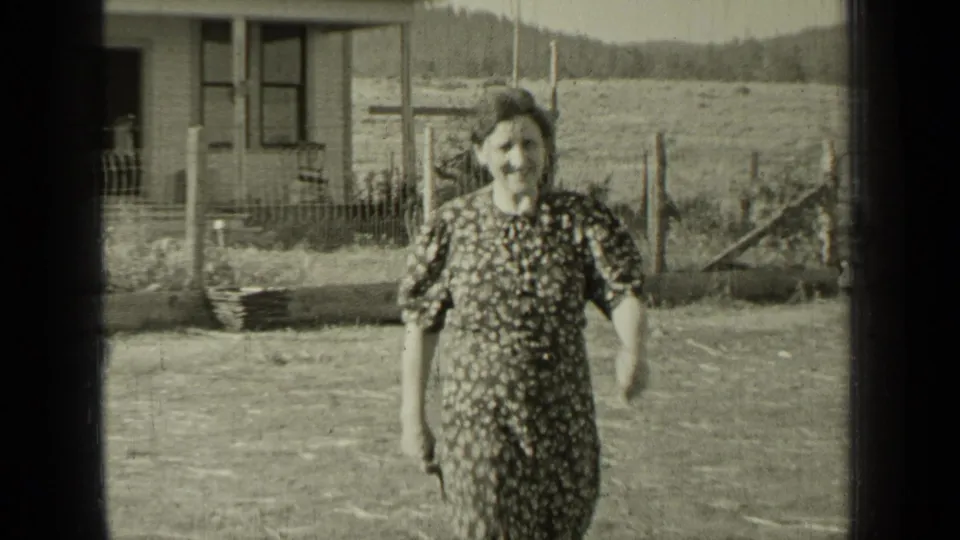 In Bend, Oregon home-movie footage from 1937, a woman in a patterned dress walks toward the camera across an open yard.