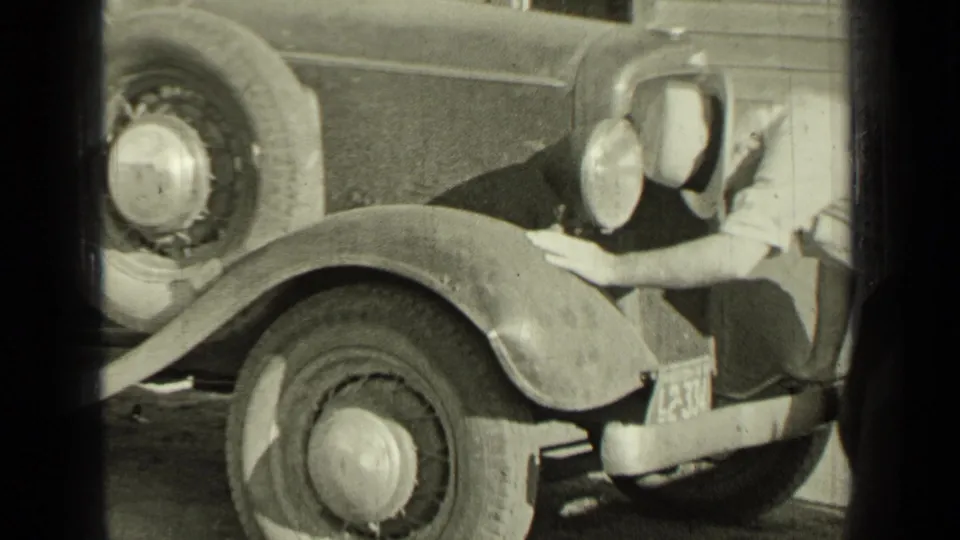 A man wearing a hat leans toward the front wheel area of a vintage vehicle in the Bend, Oregon yard scene.