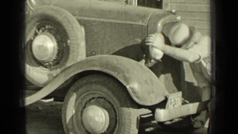 In Bend, Oregon 1937 footage, a man in a light hat appears to crank a vintage automobile with its fender, wheel, and license plate visible.