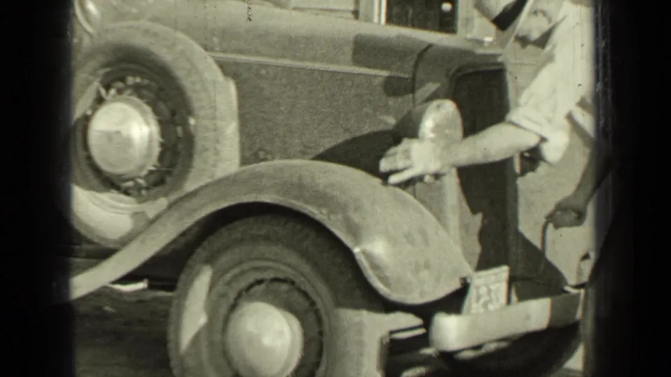 The 1937 Bend, Oregon home-movie frame shows a man beside the front of a vintage car, with wheel, fender, spare tire, and bodywork visible.