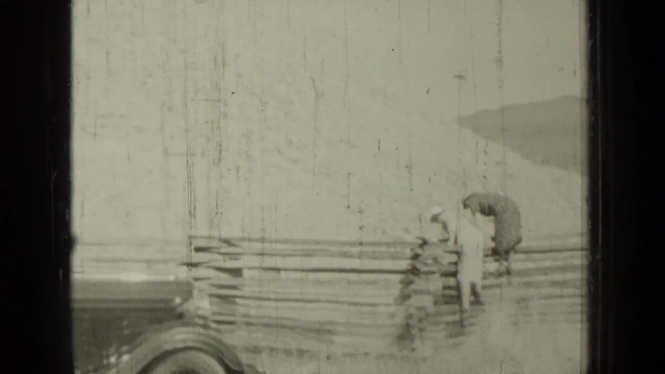 The later 1937 Bend, Oregon frame shows two women by a wooden rail fence, one bent toward the fence or ground in a rural outdoor view.