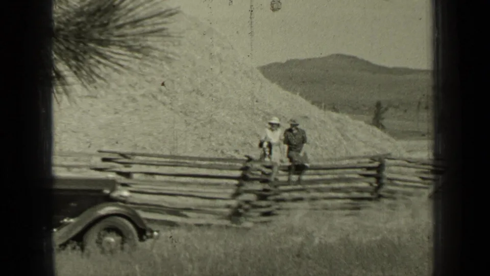 The Bend, Oregon scene shows two adults by a fence, with part of an early automobile visible against hills and open grass.