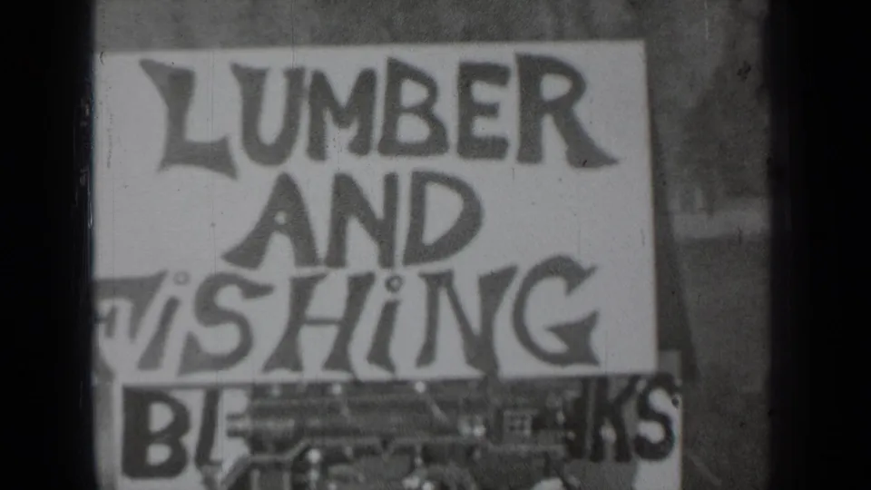 1937 Klamath, California 8mm frame showing a soft-focus hand-painted sign reading lumber and fishing, with partial text below.