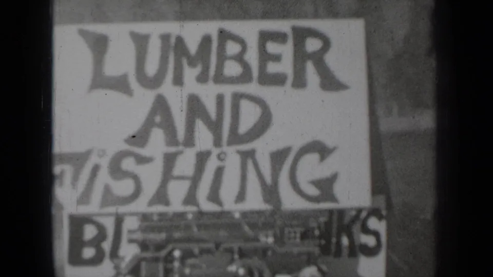 1937 Klamath, California 8mm frame showing the hand-painted lumber and fishing sign with grain, dust, and partial lower wording.