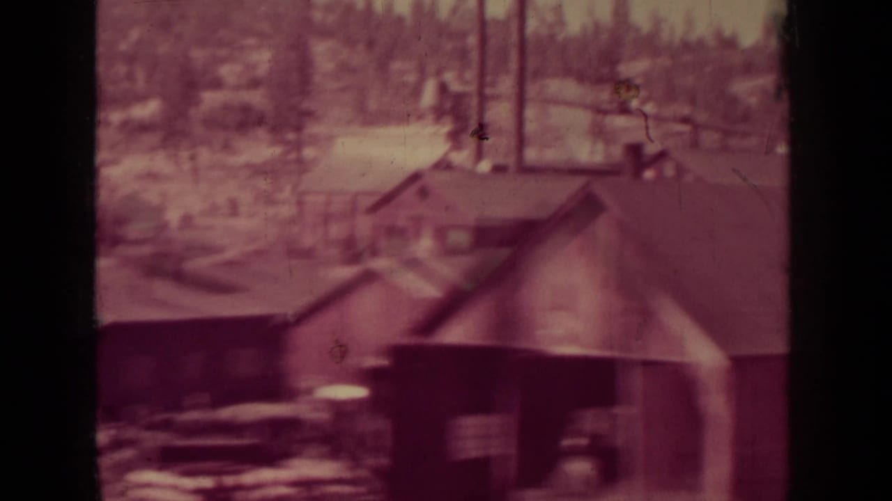 Soft 8mm view of mill rooftops, a smokestack, and wooded hills beyond.