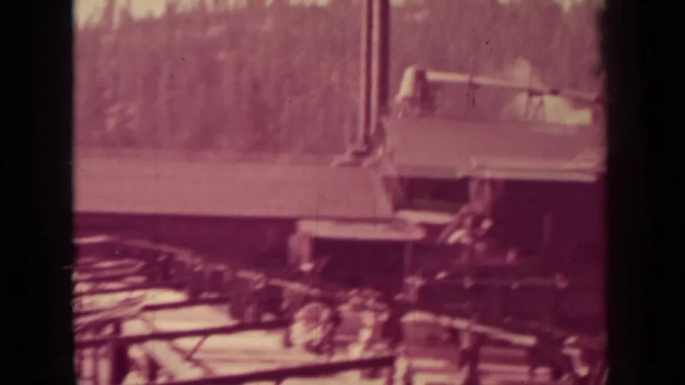 Soft 8mm view of a Klamath lumber work yard in 1937, with workers near railings, stacked material, and a large corrugated-roof building.