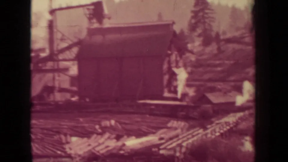 1937 Klamath, California 8mm frame showing a wooden mill building, log piles, and nearby handling structures.