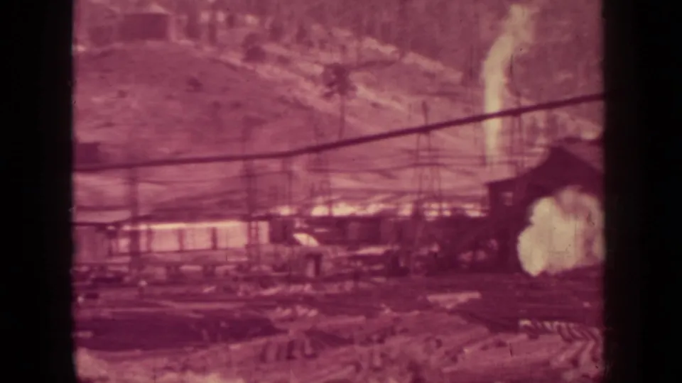 1937 Klamath, California lumber plant view with smoke, timber-handling structures, low buildings, and a forested hillside.