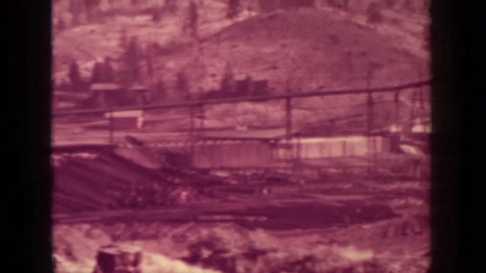 Wide 1937 Klamath lumber mill yard showing conveyors, yard structures, low buildings, and a wooded hillside beyond.