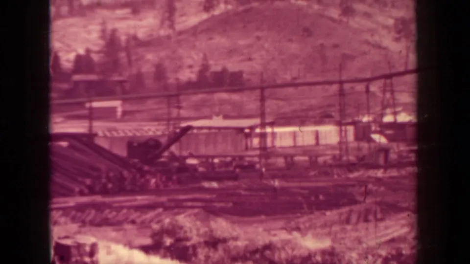 1937 Klamath lumber plant scene with conveyors, industrial buildings, yard areas, utility lines, and hillside trees.