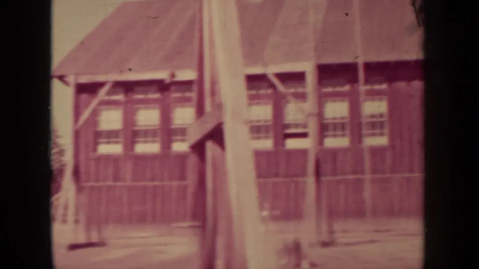 1937 Klamath, California 8mm frame showing a rustic wooden building with rows of windows at the edge of a forest clearing.