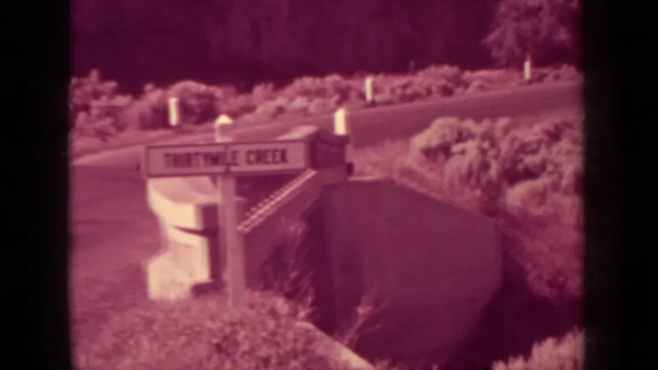 Second view of the Thirtymile Creek sign in Klamath, California, with brush, hillside, and roadside posts visible.
