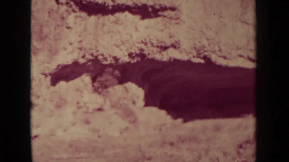 Faded 8mm home-movie frame of arid land near Klamath, California, with a dark crevice-like formation and visible film texture.