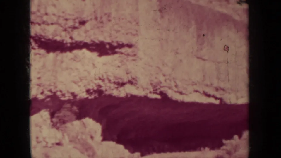 Final 8mm frame from the clip shows pale western desert terrain and a broad dark ravine-like band in faded color.