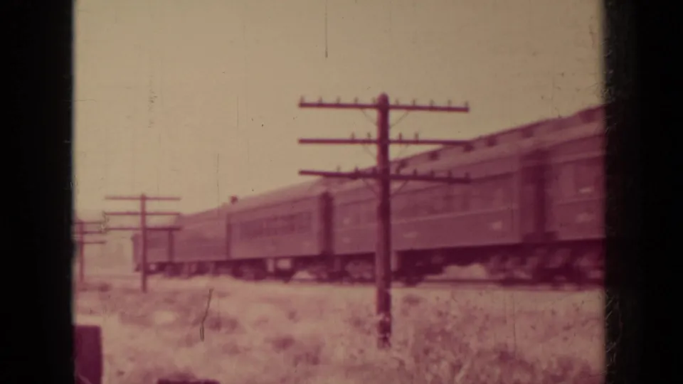 Passenger rail cars pass through a trackside landscape with utility poles in the 1937 Klamath, California home-movie clip.
