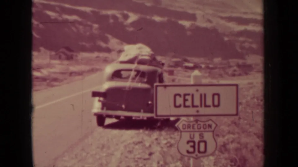 A 1930s automobile with roof luggage is parked beside a Celilo, Oregon sign and US 30 highway marker.