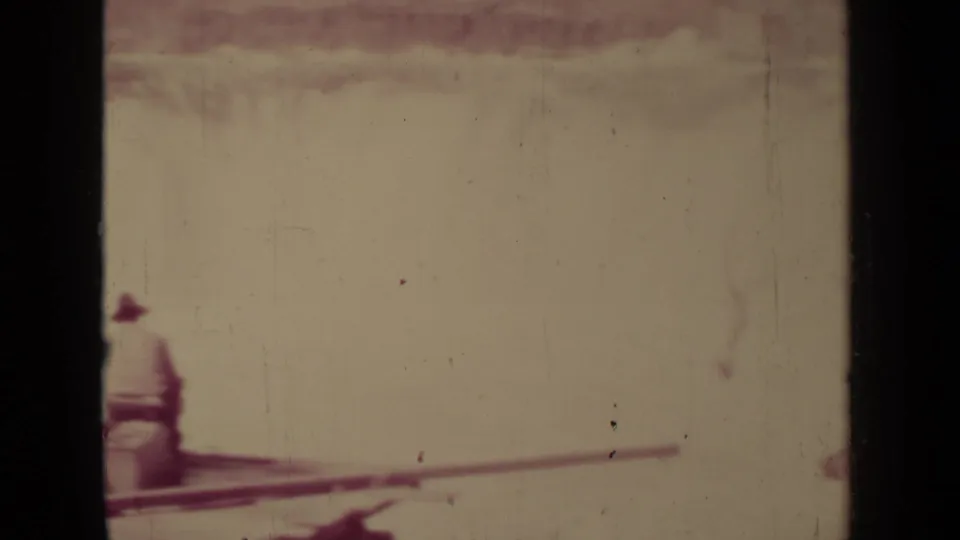 A 1937 Klamath home-movie frame shows the lower edge of a wooden overlook or railing against bright water, with strong film wear visible.
