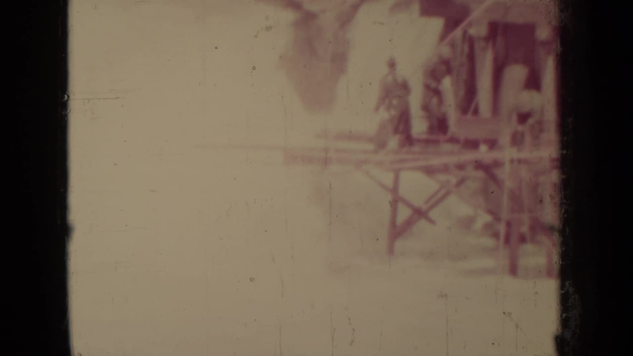 Faded view of a small wooden structure on supports with distant figures nearby.