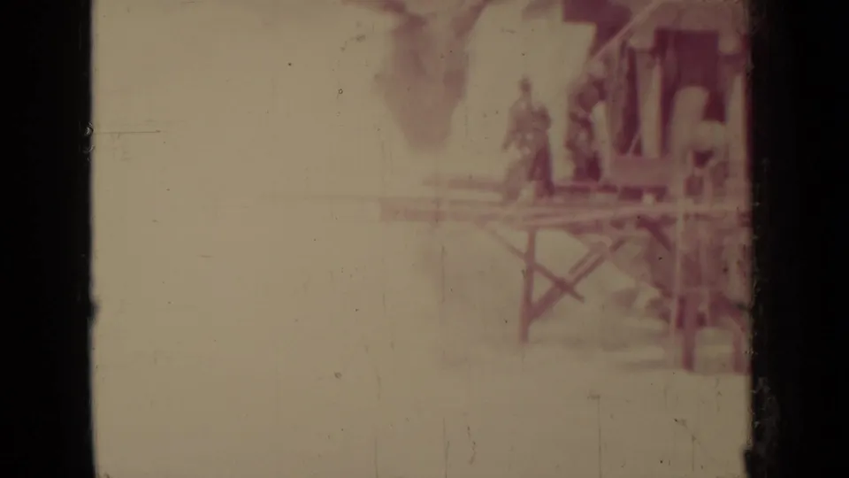 1937 Klamath, California 8mm frame showing a hazy wooden mine structure on stilts with distant people nearby.